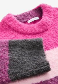 Rosa och grå randig tröja i mjukt, texturerat material. Har en hög krage och sänkt axel med en etikett inuti kragen.