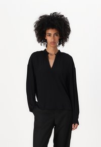 Top nero a maniche lunghe con scollo a V e un delicato dettaglio a nodo sul colletto, realizzato in tessuto liscio con una vestibilità comoda.