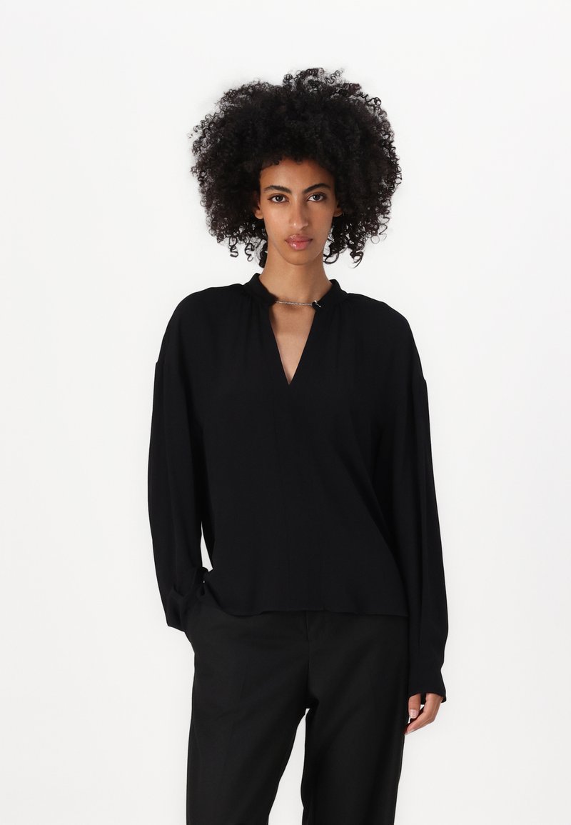 Top nero a maniche lunghe con scollo a V e un delicato dettaglio a nodo sul colletto, realizzato in tessuto liscio con una vestibilità comoda.