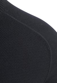 Nahaufnahme von schwarzem, strukturiertem Stoff mit einer gekrümmten Naht, die das Strickmuster und die glatte Nähte zeigt.