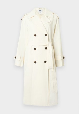 Κρεμ διπλής σειράς παλτό καμπαρντίνα με σκούρα κουμπιά, ζώνη στη μέση, επιθεωρήσεις στους ώμους και ρυθμιζόμενα λουριά στα μανίκια.