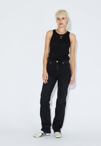 Schwarzes Trägershirt kombiniert mit hoch taillierten schwarzen Jeans aus Denim, die einen geraden Beinausschnitt und minimalistische Details aufweisen, abgerundet mit Schuhen in neutralen Farbtönen.