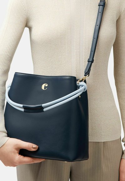 Navy leather bucket bag with light blue top handle, gold logo, and adjustable strap. Smooth texture, rounded shape, and minimalistic design.