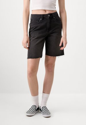 Shorts en denim noir avec un ourlet effiloché, cinq poches et une fermeture à bouton à l'avant, associés à des chaussures à motif à carreaux et des chaussettes blanches.