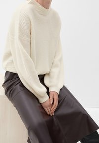 Suéter grueso de punto crema con un cuello alto y textura acanalada, combinado con una falda de cuero marrón oscuro con un acabado suave.