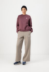 Burgundi värvi sviiter ümarate kaelustega, beežid laiad dressipüksid New Balance'i logoga ja sinised spordijalatsid. Peas must kudumüts.