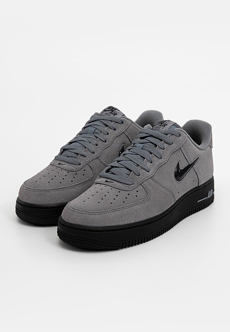 Un par de zapatillas Nike Air Force 1 grises con suelas negras y logotipos de Nike en negro, atadas y posicionadas lado a lado sobre una superficie blanca.