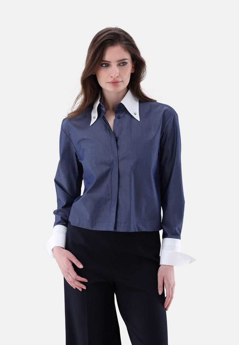 Button-up shirt in dark blue fabric with a white spread collar and cuffs. Features contrasting white accents and silver button details.