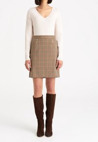 Světlý béžový žebrovaný top s dlouhým rukávem v kombinaci s hnědou kostkovanou sukní s knoflíky a tmavě hnědými semišovými kozačkami ke kolenům.