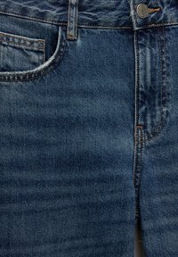 Jean en denim bleu avec poche avant, passant de ceinture, bouton métallique et coutures orange visibles sur tissu texturé.