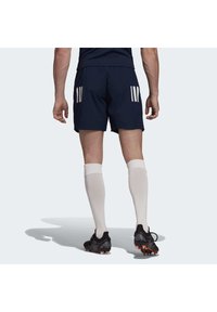 Dunkelblaue Shorts mit weißen drei Streifen, kombiniert mit knielangen weißen Socken und schwarzen Fußballschuhen mit orangefarbenen Akzenten.