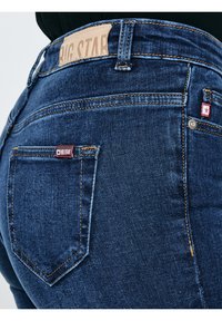 Tuvplāns tumši zilu džinsu aizmugurējā kabatā ar redzamām šuvēm un "BIG STAR" zīmola etiķeti uz jostas un kabatas.