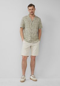 Olijfgroen kortemouwen shirt met patroon en knopen, gecombineerd met lichtbeige shorts en lichte sneakers met een gestructureerd ontwerp.