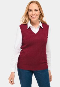 Bordeaux sweatervest met een kabelbreipatroon, V-hals ontwerp en geribde onderrand, gedragen over een wit hemd met kraag.