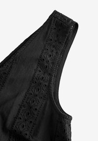 Top nero senza maniche con ricami floreali lungo il colletto e fori ad occhio, realizzato in tessuto leggero.