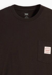 Black short-sleeve T-shirt in cotton, featuring a front pocket with a red and white label. The neckline is crew-style with ribbed texture.