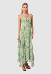 Green, flowing dress with a deep V-neck and spaghetti straps. Features a marbled texture and a high-low hem. Worn with strappy black heels.