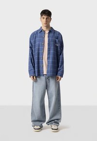 Plava karirana široka košulja, zatvara se na gumbe, nošena preko svijetlo ružičaste majice. Svijetlo plave traperice širokih nogavica, bijele tenisice s crnim detaljima.