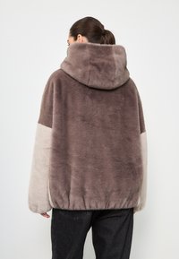 Giacca a zip in pile con una superficie morbida e texturizzata. Blocchi di colore in grigio chiaro e taupe. La vita elasticizzata completa la vestibilità rilassata.