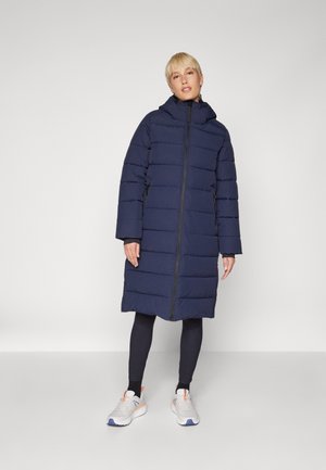 Doudoune navy avec une fermeture éclair intégrale, grande capuche et manches longues. Présente un design matelassé avec deux poches latérales.