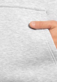 Le tissu clair du sweat-shirt gris présente une poche avant avec une main posée dessus, mettant en valeur la texture douce du matériau et son design sans couture.