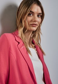 Różowa żakiet teksturowany z klapami, noszony na białym topie, o luźnym kroju i subtelnie tkanym wzorze.