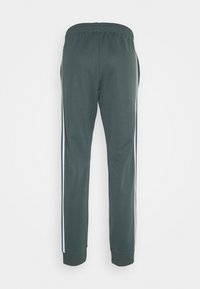 Pantaloni della tuta verde scuro con vita elastica, strisce laterali bianche, gambe affusolate e polsini a coste. Tessuto liscio con finitura opaca.