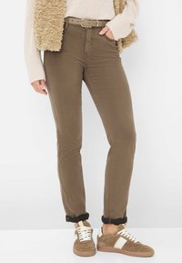 Bruine slim-fit jeans met een ontwerp voor een voorkruiszak, gecombineerd met beige suède sneakers met witte accenten en veters, met opgerolde boorden bij de enkels.