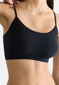 Černý bralet s tenkými nastavitelnými ramínky, vyrobený z hladké látky. Má bezešvý design a měkký elastický pás s detaily loga.