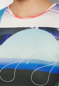 Tričko s krátkým rukávem a klasickým výstřihem z lehké tkaniny. Vyznačuje se abstraktními modro-černými vzory a bílými liniemi na přední straně.