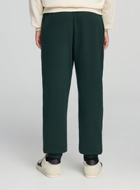 Ciemnozielone spodnie dresowe o luźnym kroju, wykonane z miękkiego materiału. Pas jest elastyczny, z prążkowanymi ściągaczami. Nosi się je z jasnymi trampkami.