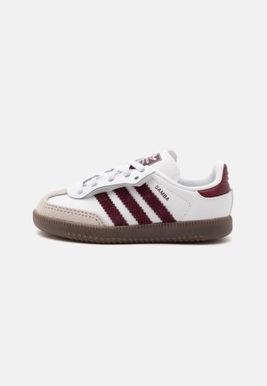 Valged ja burgundia värvi Adidas Samba tennised kummist tallaga, burgundia triipude ja paeltega ühtlasel heledal taustal.