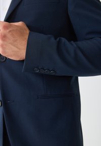 Μπλε σακάκι ναυτικού στυλ με λείο, δομημένο ύφασμα. Διαθέτει μία τσέπη, έξι σκουρόχρωμα κουμπιά στο μανίκι και μία διακριτική λάμψη.