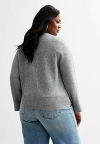 Ljusgrå tröja med ribbat avslut och manschetter, med en avslappnad passform och mjuk textur. Matchas med blå högmidjade jeans.
