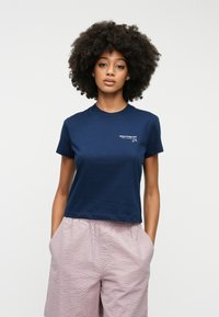 Marineblå bomulds t-shirt med rund hals og korte ærmer, præget af en hvid logo-detalje på brystet. Bæres med lyserøde strukturerede shorts.