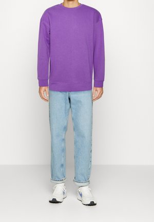 Felpa viola con maniche lunghe e collo rotondo, abbinata a jeans dritti azzurri chiari e sneakers bianche. Design semplice, senza fantasie.