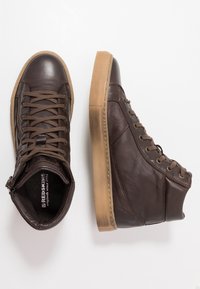 Bottes de sport montantes en cuir marron avec surface texturée, semelle en caoutchouc contrastante, lacets à l'avant et zip sur le côté pour un enfilage facile.