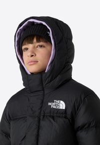 Must mustriga turritustega jope, millel on kõrge krae, lavendlivärvi vooder ja valged logosildid. Kaasas must kootud müts.