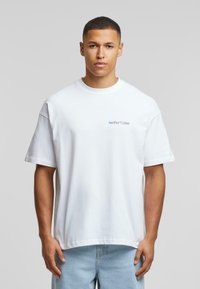 Bílý bavlněný tričko s volným střihem a krátkými rukávy. Na levé straně hrudi se nachází modré logo "Another Cotton". Měkká textura.