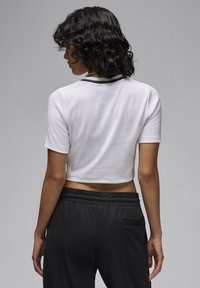 Cropped white t-shirt with short sleeves and black trim at the collar, paired with black pants featuring an elastic waistband and back pocket.