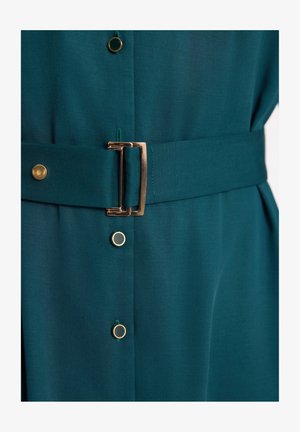 Turkusowa sukienka o teksturowym wykończeniu, z złotą paskiem z klamrą, złotymi guzikami oraz dopasowanym taliowaniem.