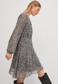 Zwart-wit gestreepte jurk met lange mouwen, doorschijnende stof en een uitlopende rok. Heeft een ronde halslijn en een vloeiende silhouet.