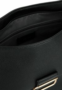 Interno di borsa in pelle nera testurizzata con una fodera in tessuto liscio; presenta un accento in metallo dorato e una tasca con zip.