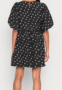 Musta mekko valkoisilla kukkakuvioilla, lyhyet puffihihat, rypistetty vyötärö ja takana avainaukko, valmistettu teksturoidusta kankaasta.