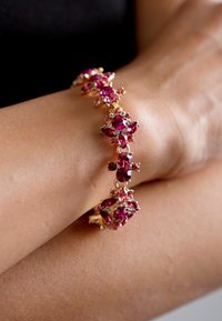 Bracciale con gemme rosa e dettagli in metallo tono oro, caratterizzato da varie forme di pietre e elementi di design intricati.
