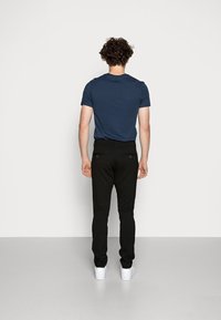 Marinblå kortärmad t-shirt, svarta slim-fit byxor och vita sneakers. Materialet verkar slätt; inga synliga mönster eller dekorationer.