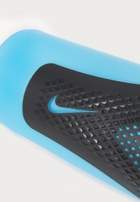Nike vízpalack, amely matt kék testtel, texturált fekete markolattal rendelkezik gyémántmintákkal, és oldalt egy kis kék logó díszíti.