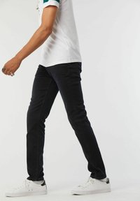 Jeans en denim noir avec une coupe slim, portés avec un t-shirt blanc et des baskets blanches. Texture lisse, design traditionnel à 5 poches, détails minimaux.
