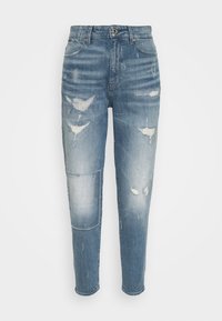 Světle modré džínové kalhoty s volným střihem, s opotřebovanými místy a nášivkou na levé noze. Klasický střih s pěti kapsami a zipem.