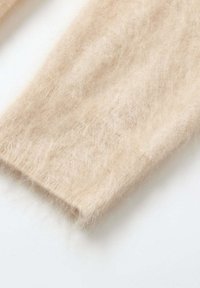 Maglione lavorato a maglia di un colore beige chiaro, con una texture morbida e pelosa e maniche lunghe con orlo dritto. Realizzato in un materiale caldo e delicato.